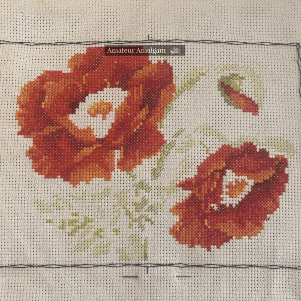 cross stitching canvas partially filled in - the image appears to be two open poppy flowers and a closed bud, the outline of the leaves can be seen